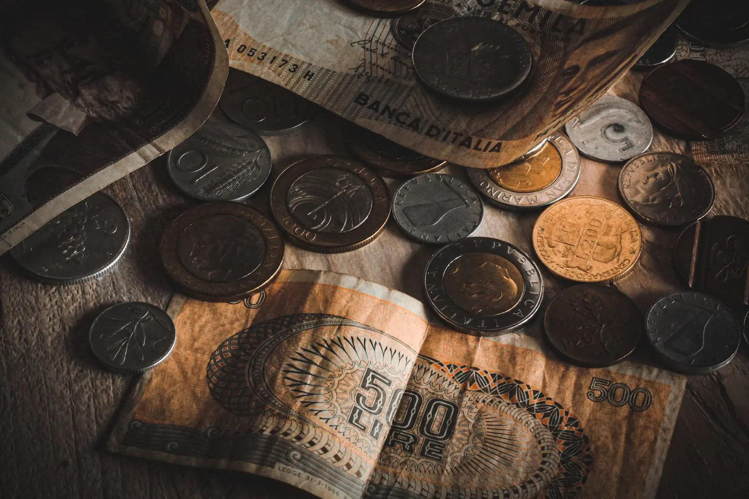 Worn vintage Italian banknotes and coins under angled light with visible folds and surface wear